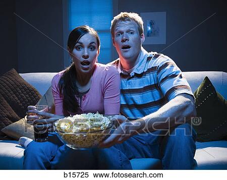 Couple on sofa with bowl of popcorn looking shocked View Large Photo Image Stock Photography - Couple on sofa with bowl of popcorn looking shocked. Fotosearch