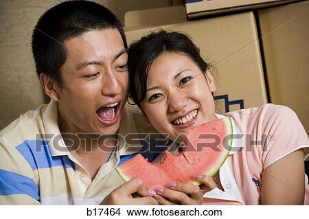 Couple sharing watermelon and smiling with cardboard boxes in background View Large Photo Image Picture - Couple sharing watermelon and smiling with cardboard boxes in background. Fotosearch