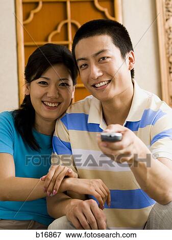 Stock Photo - Couple sitting on sofa watching television smiling. Fotosearch