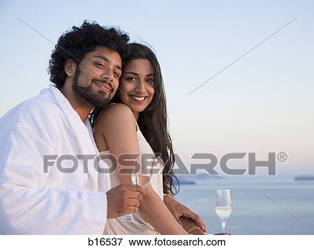 Couple sitting outdoors with champagne flutes and scenic background smiling and snuggling View Large Photo Image Stock Photo - Couple sitting outdoors with champagne flutes and scenic background smiling and snuggling. Fotosearch