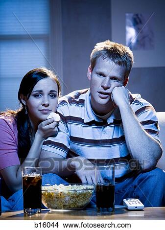 Couple watching television with bowl of popcorn and tissue looking sad View Large Photo Image Picture - Couple watching television with bowl of popcorn and tissue looking sad. Fotosearch