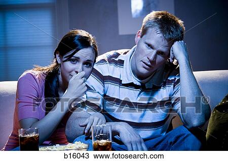 Stock Image - Couple watching television with bowl of popcorn looking sad. Fotosearch