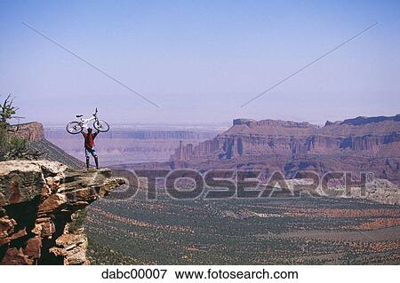 Cyclist on cliff holding bicycle above head with red rock View Large Photo Image Stock Photo - Cyclist on cliff holding bicycle above head with red rock. Fotosearch
