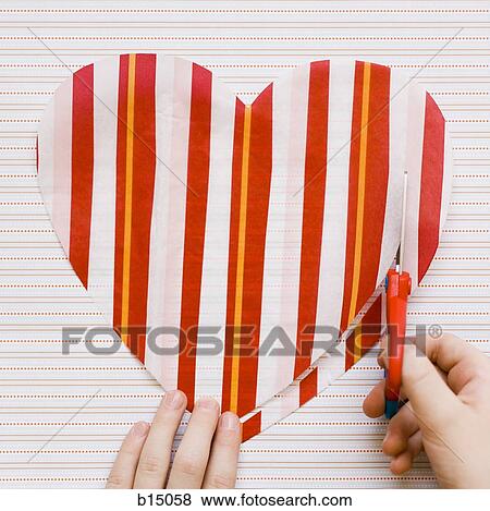 Stock Photo - Detailed view of person cutting striped heart with scissors. Fotosearch
