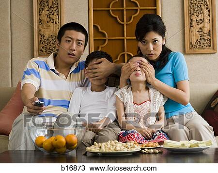 Stock Image - Family watching television with parents covering children's eyes. Fotosearch