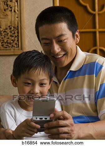 Father and son looking at portable electronic device View Large Photo Image Picture - Father and son looking at portable electronic device. Fotosearch
