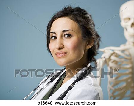 Stock Photo - Female doctor smiling with skeleton in background. Fotosearch