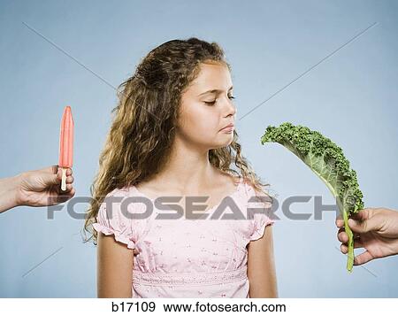 Girl deciding between Popsicle and green leafy vegetable View Large Photo Image Stock Photo - Girl deciding between Popsicle and green leafy vegetable. Fotosearch