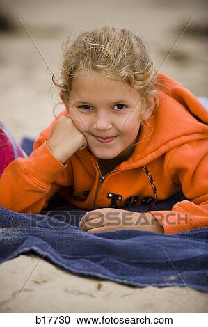 Stock Image - Girl lying on beach towel in sand smiling. Fotosearch