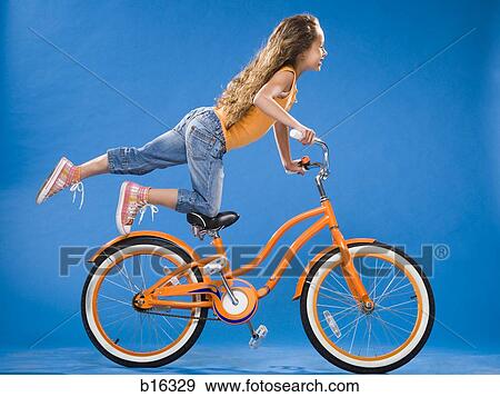 Girl on orange bicycle kneeling on seat with foot up View Large Photo Image Stock Photo - Girl on orange bicycle kneeling on seat with foot up. Fotosearch