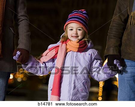 Stock Image - Girl outdoors in winter smiling holding hands with adults. Fotosearch