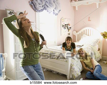 Girl singing into hairbrush in bedroom with girlfriends laughing View Large Photo Image Picture - Girl singing into hairbrush in bedroom with girlfriends laughing. Fotosearch