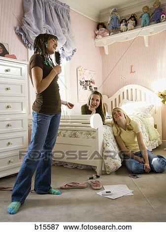 Girl singing into hairbrush in bedroom with girlfriends laughing View Large Photo Image Stock Photo - Girl singing into hairbrush in bedroom with girlfriends laughing. Fotosearch