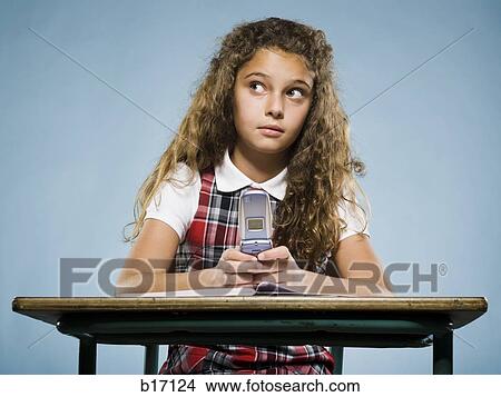 Girl sitting at desk with workbook and cell phone View Large Photo Image Picture - Girl sitting at desk with workbook and cell phone. Fotosearch