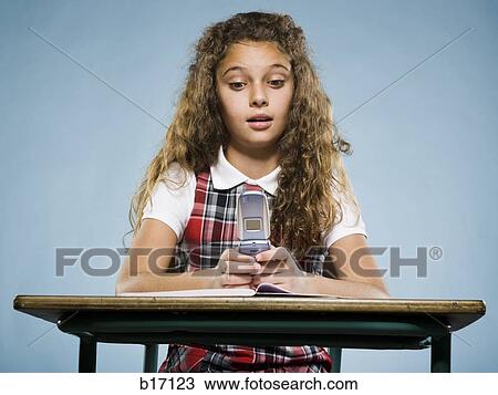 Girl sitting at desk with workbook and cell phone View Large Photo Image Stock Image - Girl sitting at desk with workbook and cell phone. Fotosearch