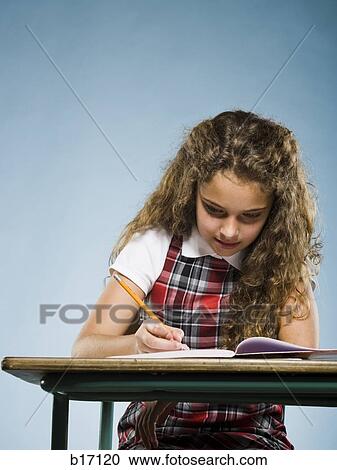 Stock Image - Girl sitting at desk with workbook writing. Fotosearch
