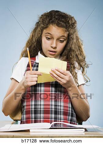 Girl sitting at desk with workbook reading note View Large Photo Image Stock Photo - Girl sitting at desk with workbook reading note. Fotosearch
