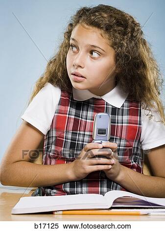 Girl sitting at desk with workbook hiding cell phone View Large Photo Image Stock Photography - Girl sitting at desk with workbook hiding cell phone. Fotosearch