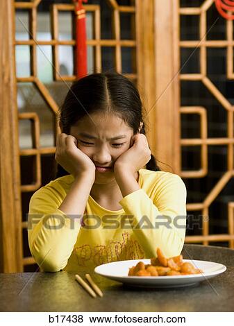 Girl sitting at table looking at plate of food with disgust View Large Photo Image Stock Photo - Girl sitting at table looking at plate of food with disgust. Fotosearch