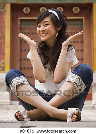 Stock Photography - Girl sitting cross legged outdoors smiling with hands up. Fotosearch