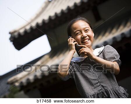 Girl standing outdoors with cell phone in front of pagoda smiling View Large Photo Image Stock Photo - Girl standing outdoors with cell phone in front of pagoda smiling. Fotosearch