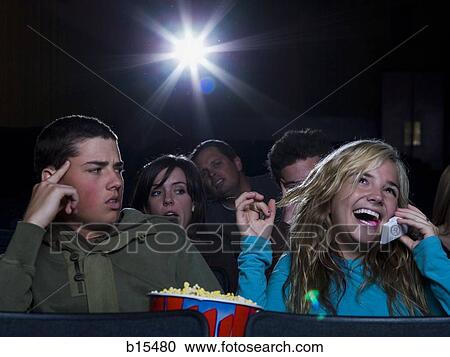 Girl talking on cell phone at movie theater with annoyed boy View Large Photo Image Stock Image - Girl talking on cell phone at movie theater with annoyed boy. Fotosearch