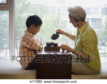 Stock Photo - Grandmother and grandson sitting cross legged drinking tea. Fotosearch