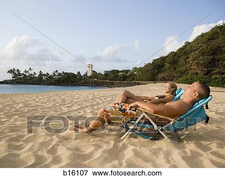 Stock Photo - Man and woman reclining in chairs on beach. Fotosearch