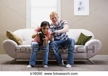 Man and woman sitting on sofa playing video games laughing View Large Photo Image Stock Image - Man and woman sitting on sofa playing video games laughing. Fotosearch