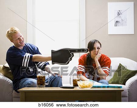 Stock Photograph - Man and woman sitting on sofa watching football. Fotosearch