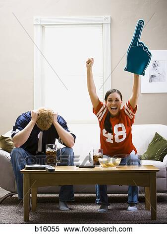 Stock Photography - Man and woman sitting on sofa watching football smiling and cheering. Fotosearch