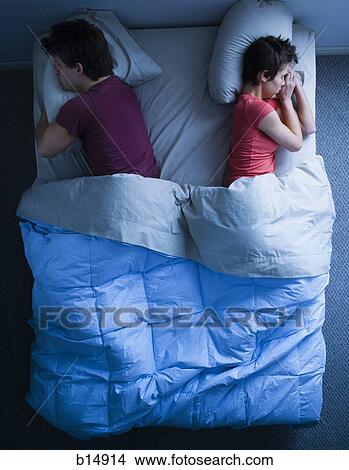 Picture - Man and woman sleeping in bed with backs to each other. Fotosearch