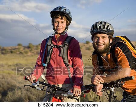 Picture - Man and woman with bicycles and helmets outdoors smiling. Fotosearch