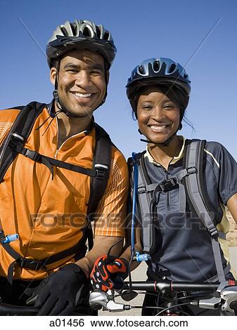Stock Photograph - Man and woman with bicycles and helmets outdoors smiling. Fotosearch