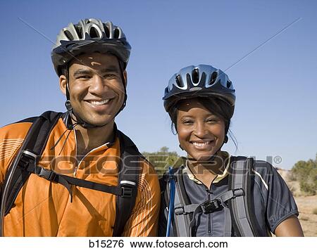 Stock Photograph - Man and woman with bicycles and helmets outdoors smiling. Fotosearch
