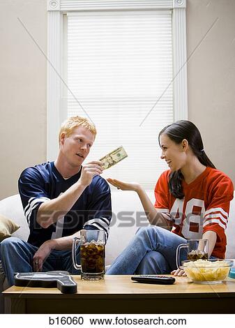 Stock Image - Man giving woman money both in football jerseys. Fotosearch