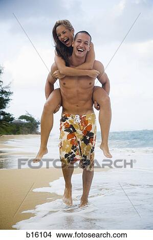 Man giving woman piggyback ride on beach View Large Photo Image Picture - Man giving woman piggyback ride on beach. Fotosearch