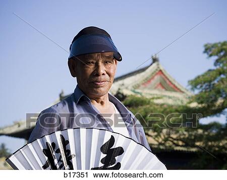 Stock Image - Man holding Chinese fan with pagoda and blue sky in background. Fotosearch