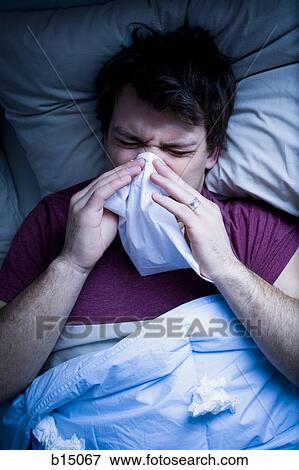 Stock Photo - Man in bed blowing nose with tissue. Fotosearch