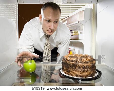 Man in refrigerator reaching for green apple looking at chocolate cake View Large Photo Image Stock Photo - Man in refrigerator reaching for green apple looking at chocolate cake. Fotosearch