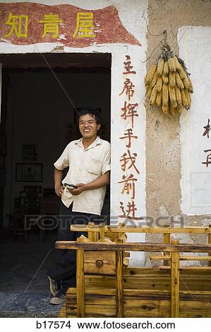 Man leaning on door frame with Chinese characters and corn hanging View Large Photo Image Picture - Man leaning on door frame with Chinese characters and corn hanging. Fotosearch