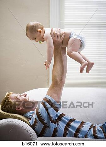 Man lying down on sofa holding baby in air View Large Photo Image Stock Image - Man lying down on sofa holding baby in air. Fotosearch