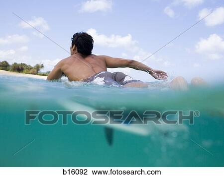 Man lying on surfboard in water View Large Photo Image Stock Image - Man lying on surfboard in water. Fotosearch