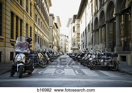 Man on motorcycle looking back at rows of parked motorcycles on street with old buildings View Large Photo Image Stock Image - Man on motorcycle looking back at rows of parked motorcycles on street with old buildings. Fotosearch