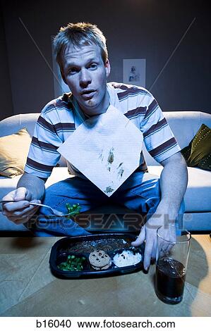Stock Image - Man on sofa with frozen dinner and napkin with food. Fotosearch