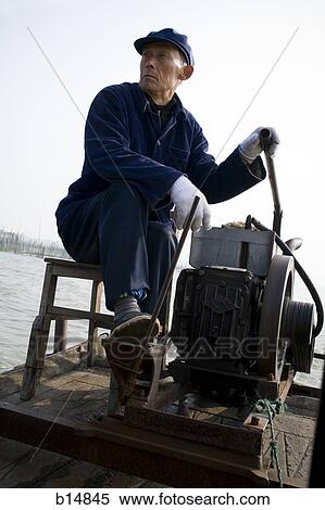 Man sitting on stool outdoors on the water with machine View Large Photo Image Stock Photography - Man sitting on stool outdoors on the water with machine. Fotosearch