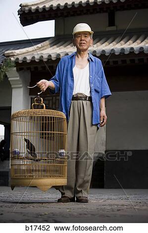 Stock Image - Man standing outdoors with bird in cage. Fotosearch