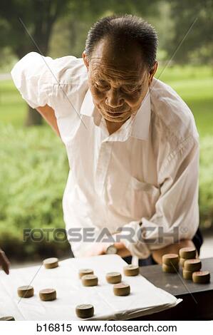 Man standing over board game outdoors concentrating View Large Photo Image Stock Photography - Man standing over board game outdoors concentrating. Fotosearch