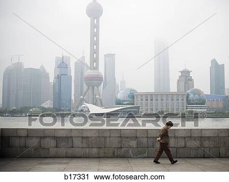 Stock Image - Man walking along waterfront with city skyline. Fotosearch