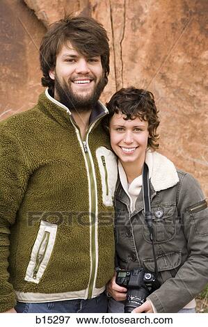 Man with beard and woman with camera hugging outdoors with red rock in background View Large Photo Image Stock Photo - Man with beard and woman with camera hugging outdoors with red rock in background. Fotosearch